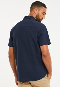 Camisa de manga corta azul marino hecha de lino con cuello, que presenta una textura suave y un dobladillo curvado en la parte posterior.