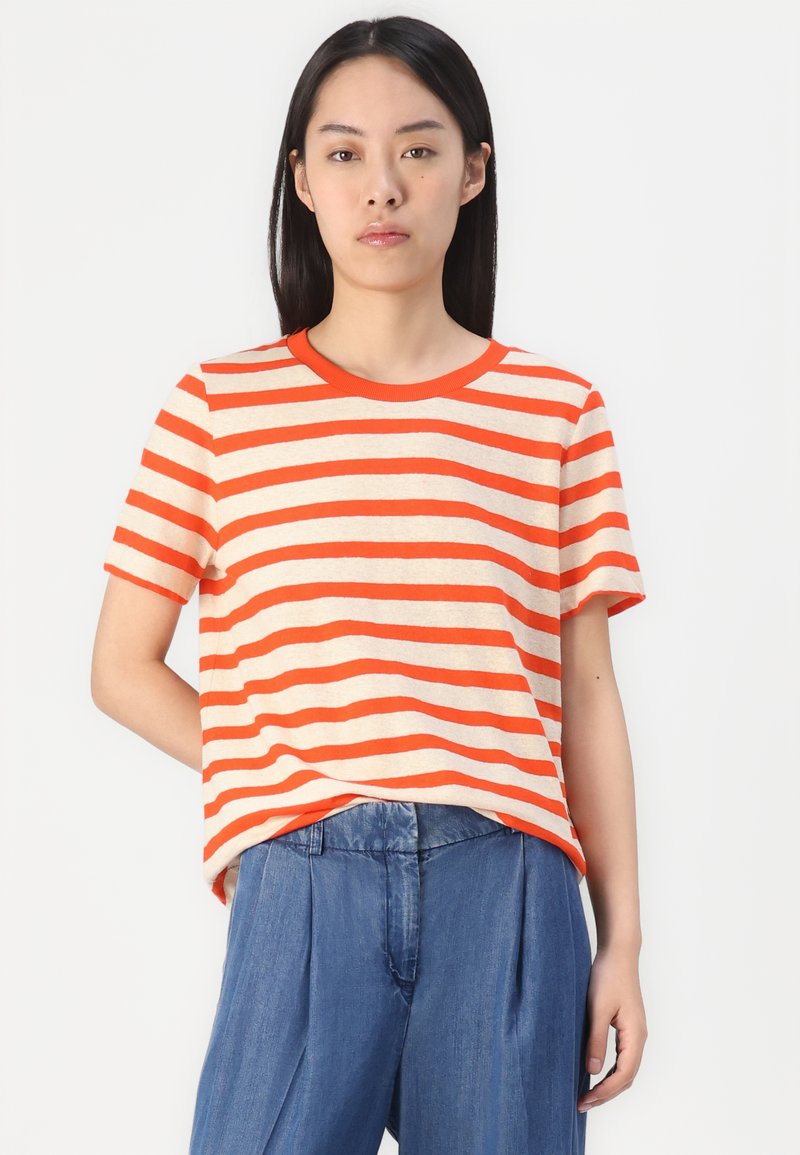 Gestreiftes T-Shirt in hellbeige und kräftigem Orange, kurze Ärmel, Rundhalsausschnitt, lässige Passform, kombiniert mit lockerer blauer Hose.