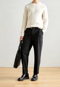 Gerippter cremefarbener Pullover, schwarze plissierte Hose, schwarze Lederschuhe und eine Schultertasche. Minimalistisches Design mit neutralen Farben und Texturen.