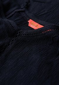 Navyblauwe getextureerde top met een geraffineerde halslijn, met een haakwerk trim en een opvallend rood merklabel.