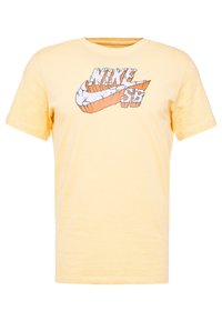 Camiseta de algodón amarilla con un gráfico del logo de Nike SB en blanco y naranja en la parte frontal. Mangas cortas y un diseño clásico de cuello redondo.