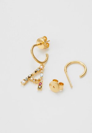 Boucles d'oreilles créoles en or, dont une est ornée d'un pendentif lettre A serti de pierres précieuses, avec deux fermoirs papillon dorés sur fond blanc.