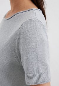 Hellgrauer kurzärmeliger Pullover mit Rundhalsausschnitt. Gewebte Textur, sichtbare Nähte und gerippte Bündchendetails an den Ärmeln.