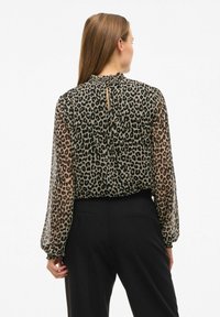 Blusa trasparente con motivo leopardato, scollatura arricciata e polsini elasticizzati, abbinata a pantaloni neri. Vista posteriore mostrata.