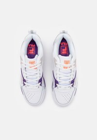 Baskets blanches et violettes FILA avec logo orange sur semelles intérieures violettes, vues de dessus, lacées et placées côte à côte sur fond blanc.