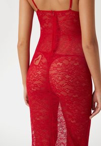 Red lace dress featuring thin straps, a zip closure at the back, and a heart-shaped detail. The fabric has a delicate and sheer texture.
