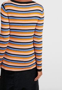 Pull en maille côtelée à manches longues avec des rayures horizontales dans les tons pêche, orange, bleu et noir. Encolure et ourlet noirs, coupe ajustée.