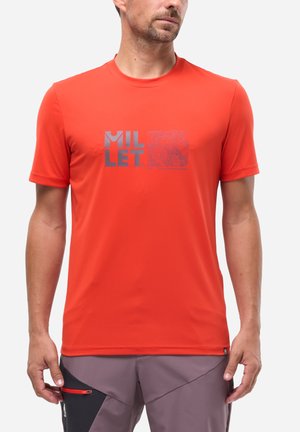 Homme portant un t-shirt à manches courtes orange vif avec un logo "MILLET" gris et un carré à motifs, associé à un pantalon gris et noir avec une fermeture éclair rouge.