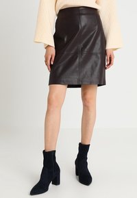 Jupe en cuir marron avec des détails de coutures et une coupe droite, associée à des bottines en suède bleu marine avec un talon bloc.