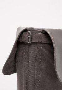 Bota de ante gris con parte superior de cuero liso, que cuenta con un cierre de hebilla y forro de tejido texturizado. Detalles cosidos a lo largo de las costuras.