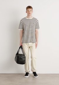Striped black and white t-shirt, cream pants, black leather bag, and black shoes. Simple design with smooth textures and neutral colors.