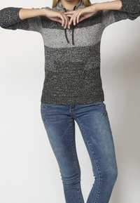 Szary i czarny sweter z dzianiny o teksturowanym wykończeniu, z kapturem na sznurki i przednią kieszenią, w zestawieniu z niebieskimi dopasowanymi dżinsami.