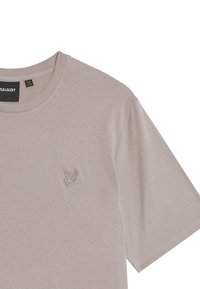 T-shirt in cotone beige chiaro con colletto a girocollo e maniche corte. Presenta un piccolo logo ricamato sul lato sinistro del petto. Texture liscia.