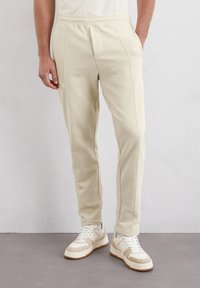 Crèmekleurige fleece joggers met een slim fit, elastische tailleband en contrasterende stiksels, in combinatie met witte en beige sneakers.