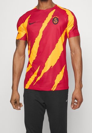 Homme portant un maillot de football Galatasaray avec un design d'empreinte de griffes rouge et jaune, logo Nike, et blason de l'équipe sur la poitrine.