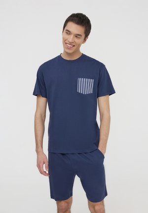 T-shirt in cotone blu navy con maniche corte e taschino sul petto, caratterizzato da righe verticali bianche; abbinato a pantaloni corti coordinati.