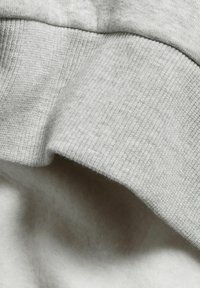 Vaaleanharmaa collegekangas, jossa on teksturoitu ribbireuna ja pehmeä sisäpinta. Pintaa koristavat hienot laikut.