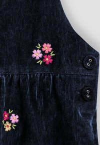 Dunkelblaues Cordstoff mit gestickten rosa, roten und gelben Blumen sowie zwei passenden runden Knöpfen mit Metallösen.