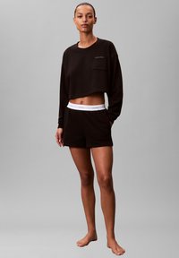 Czarna krótka bluza z kieszenią na piersi i białym logo. W zestawie z czarnymi szortami z białym paskiem z logo.