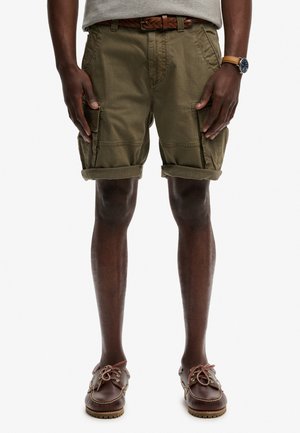 Man draagt opgerolde olijfgroene cargoshorts, een bruine gevlochten riem, bruine leren bootschoenen en een polshorloge met een bruine leren band.
