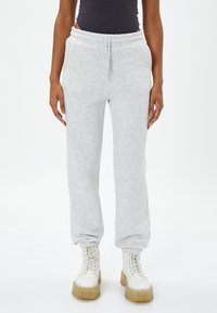 Pantalones de chándal grises claros, hechos de una tela suave, con una cinturilla elástica y cordón ajustable, y puños ajustados, combinados con botas blancas de cordones.