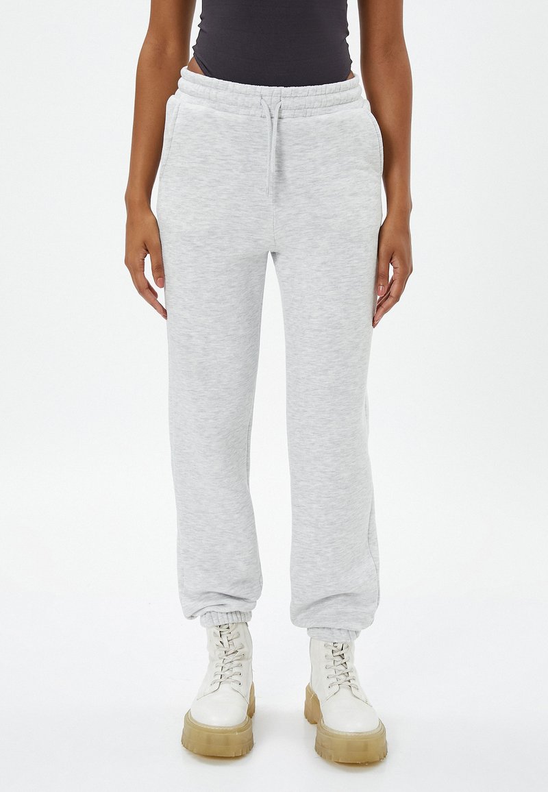 Pantalones de chándal grises claros, hechos de una tela suave, con una cinturilla elástica y cordón ajustable, y puños ajustados, combinados con botas blancas de cordones.