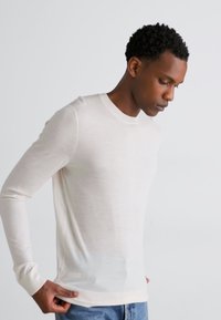Ilgais rankovės marškiniai su apvaliu kaklu, off-white spalvos, pagaminti iš lengvos medžiagos. Savybės: įrengti rausvi rankogaliai ir pritaikytas dizainas. Suderinta su mėlynomis džinsais.
