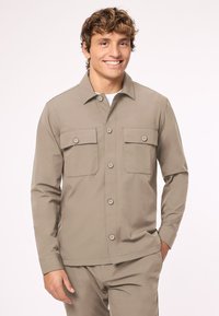 Leichte Herrenjacke in Hellbraun mit langen Ärmeln, einem Kragen, zwei Brusttaschen und Knopfverschluss, gefertigt aus glattem Stoff.