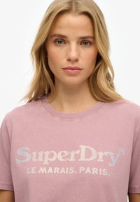 Lyserød bomulds T-shirt med rund halsudskæring, prydet med et glimrende "SuperDry" logo i flerfarvede rhinsten og teksten "LE MARAIS. PARIS."