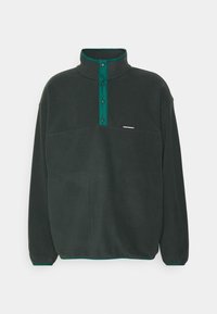 Mørkegrøn fleecepullover med høj krave, trykknapper og en forlommek. Har kontrasterende teal-detaljer. Blød tekstur.
