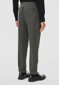 Szare, miękkie spodnie o luźnym kroju, z elastycznym pasem i zwiniętymi mankietami, zestawione z czarnymi, wypastowanymi butami.