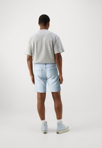 Svetle modré denimové šortky a šedé tričko s krátkým rukávem, zobrazené zezadu. Šortky mají dvě zadní kapsy a pohodlný střih.