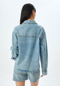 Ljusblå denimjacka med en avslappnad passform, med klassisk krage, synliga sömmar och uppvikta ärmar. Matchas med matchande denimshorts.