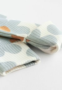 Țesătură cu striații în nuanțe de albastru pastel și crem, cu modele circulare mari și accente portocalii, având o textură moale și margini răsucite.