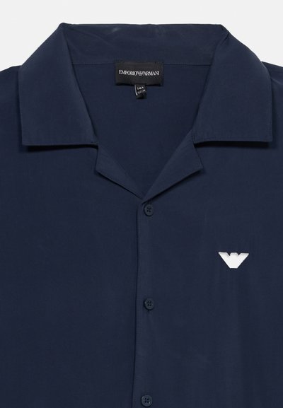 Πουκάμισο σε ναυτικό μπλε με κουμπιά και μικρό γιακά, με το λευκό λογότυπο αετού Emporio Armani στο στήθος.