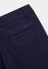 Tamnoplave hlače glatke teksture, s stražnjim džepom i izvezenim "Guess" logotipom u svijetloplavoj boji. Dizajn ravnog struka.