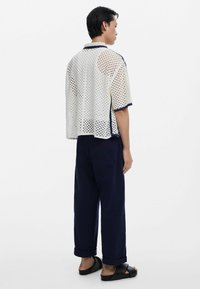 Kurzärmliges, locker sitzendes Hemd aus weißem Mesh mit Karomuster, kombiniert mit navyfarbenen Hosen. Minimalistisches Design mit Kontrastnähten.