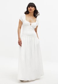 Vit maxiklänning med korta volangärmar, smocksömmad bodice, en nyckelhålsöppning fram och svängande kjol. Lättviktig tyg.