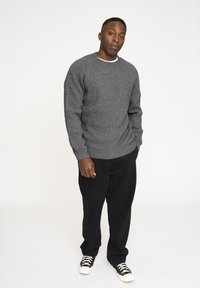 Grå ribbet striktrøje med rund halsudskæring, parret med sorte løstsiddende bukser og sorte sneakers med hvide snørebånd. Simpelt design, ingen mønstre.
