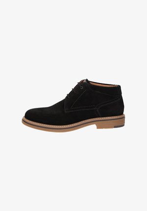 Stivaletto in suede nero con suola in gomma marrone chiaro, chiusura con lacci e dettagli di cucitura visibili su sfondo bianco.