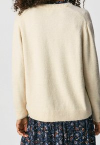 Cream-colored sweater made of soft, textured fabric with ribbed cuffs and hem; features a relaxed, boxy shape.