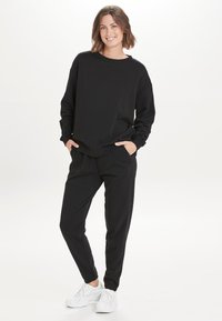 Sort sweatshirt med lange ærmer, afslappet pasform. Kombineret med sorte sweatpants, med tapered ben design. Hvide sneakers fuldender outfittet.