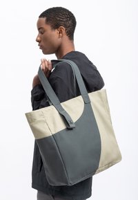 Tote tas in beige en donkergroene canvas, met stevige schouderbanden, een soepele textuur en een gebogen vormgeving aan de bovenkant.