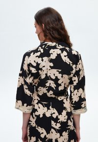 Top in stile kimono nero con stampa botanica crema, maniche 3/4 e bordo in pizzo all'orlo. Tessuto morbido con taglio rilassato.