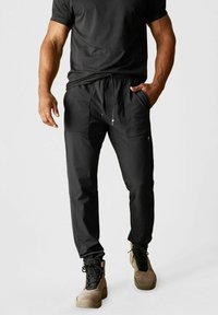 Schwarze, leichte Jogginghosen mit elastischem Bund, Kordelzug, zwei seitlichen Taschen und zulaufenden Beinen. Getragen mit sandfarbenen Militärstiefeln.