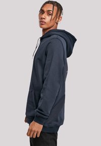 Navy blue hoodie in soft material with adjustable drawstrings, front pocket, and ribbed cuffs. Features a modern fit and textured surface.