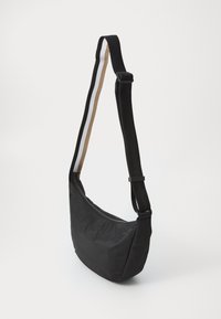Sac en nylon noir en forme courbée, doté d'une fermeture éclair et d'une sangle avec des rayures noires, blanches et brunes.