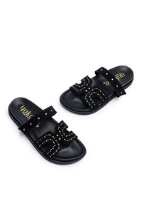 Infradito nere in suede, con due cinturini decorati con borchie dorate e un design con lettere audaci. Suola liscia e piatta per il massimo comfort.