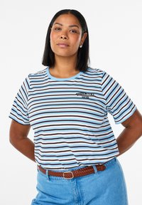 Triibuline T-särk helesiniste, valgete ja pruunide horisontaalsete joontega, ümara kaelusega, lühikeste varrukatega, millel on tikitud "ESSENTIAL 1979" detail.