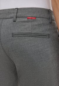 Grijze stoffen broek met een ritssluiting achterzak en een rode "JOOP! JEANS" label boven de zak, met een gestructureerde afwerking.